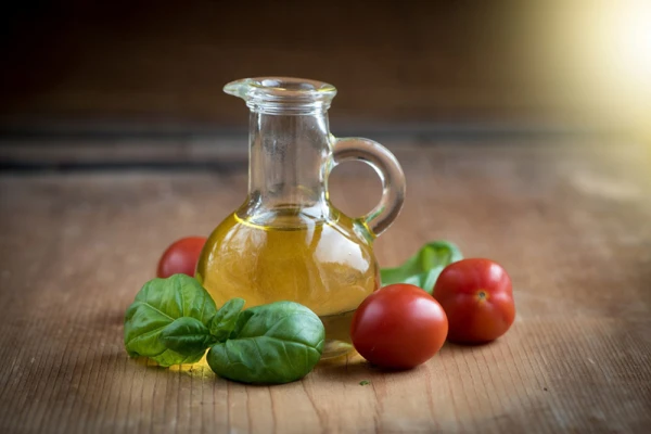 Une petite carafe d'huile entourée de tomates et de basilic